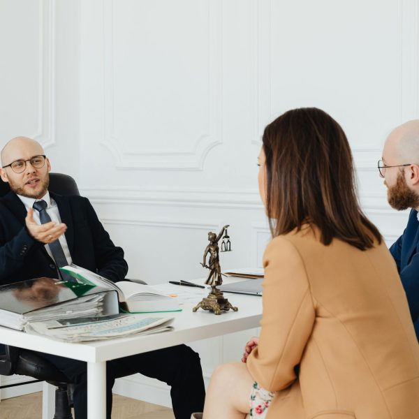 Photo by Photo By Kaboompics.com httpswww.pexels.comphotoa-couple-talking-to-a-lawyer-7876315 Lawyer talking a client sitting at the office